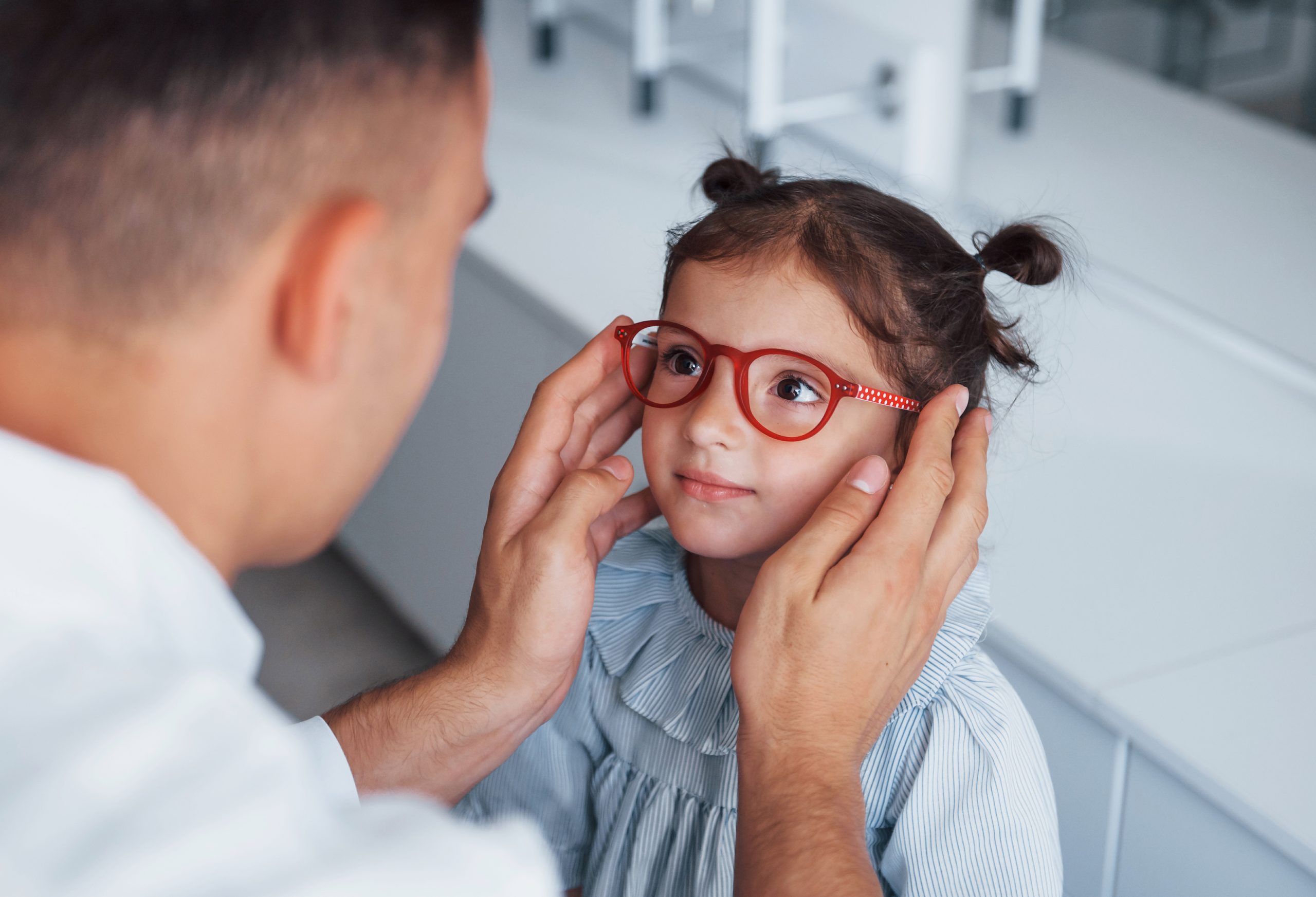 little girl trying on glasses with the help of a doctor